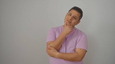 Lavanta gömlekli düşünceli genç bir İspanyol beyaz bir arka plana karşı duruyor, dalgın görünüyor..