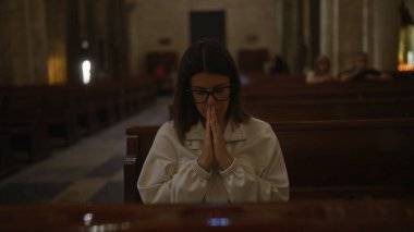 Gözlüklü, genç, güzel bir İspanyol kadın İtalya 'da loş bir Hıristiyan kilisesinde dindar bir şekilde dua ediyor..