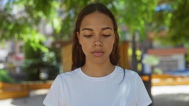 Güneşli bir günde şehir geçmişiyle şehir parkında gülümseyen genç bir kadın.