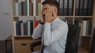 Ofis ortamında çalışan genç bir adam, profesyonel bir ortamda çalışırken duygularını belli ederek stresli ve endişeli görünüyor.