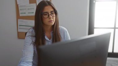 Ofiste çalışan bir kadın stresli ve hayal kırıklığına uğramış görünüyor. Etrafı doküman ve çizelgelerle çevrili bir bilgisayarla çevriliyken modern kapalı bir işyerinde çalışıyor..