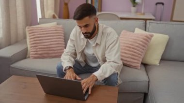 Evde, oturma odasında dizüstü bilgisayarda çalışan genç bir İspanyol, bilgisayarını kapatıp kameraya gülümsemeden önce rahat ve modern bir iç mekan ortamı sergiliyor..