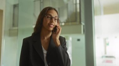 Ofiste kapalı yumruklarla kutlama yapan bir kadın telefona bakıyor, gözlük ve takım elbise giyiyor, heyecan ve başarı sergiliyor..