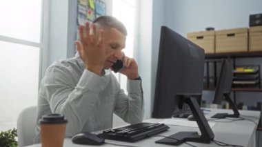 Telefonda konuşan adam ofis masasında hayal kırıklığına uğramış bir şekilde bilgisayar, kağıt kahve fincanı ve organize bir iç mekan ile konuşuyor.