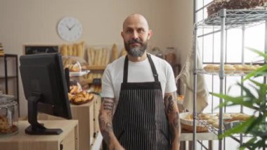 İspanyol bir adam buraya gelip bir pastaneye jest yapıyor. Etrafı pişmiş mallarla çevrili ve siyah önlük giyiyor.