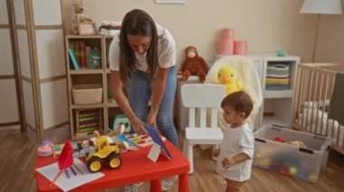 Oyuncak ve bebek odası dekorlarıyla dolu rahat yatak odasında bebekle oynayan, aile sevgisini ve sıcaklığını gösteren bir kadın..