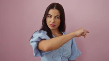 Esmer saçlı ve mavi bluzlu genç bir kadın soyutlanmış pembe arka planda duruyor.