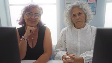 Ofiste birlikte çalışan olgun kadınlar, içeride iş yapan iki yaşlı kadın çalışan, biri gözlüklü ve ikisi de bilgisayar ekranlarına odaklanmış.