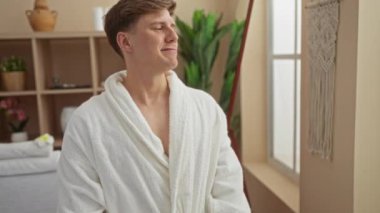 Beyaz bir bornozla kaplıcada dinlenen genç bir adam. Etrafı iç mekan bitkileriyle ve zarif dekorlarla çevrili. Huzurlu bir sağlık deneyimiyle eğleniyor.