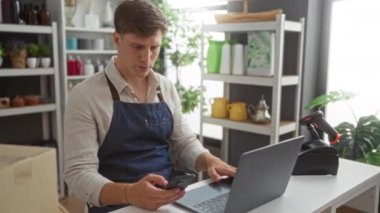 Genç adam akıllı telefon ve dizüstü bilgisayar kullanarak ev dekorasyonu mağazasında çalışıyor.