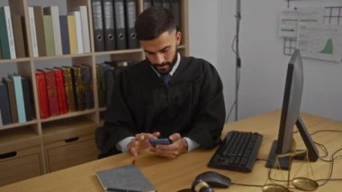 Yargıç cüppeli genç İspanyol adam ofisinde oturuyor, cep telefonunu kontrol ediyor, masada yasal kitaplar, bilgisayarlar ve teraziler var.