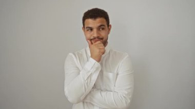Beyaz gömlekli genç İspanyol bir adam, beyaz bir arkaplanda izole edilmiş. Düşünceli bir şekilde bir fikir öne süren anlamlı jestler yapıyor..