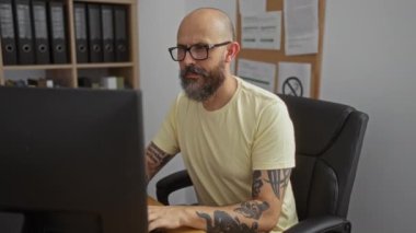 Dövmeli İspanyol bir adam ofiste çalışıyor, odaklanmış ve sonra yorgun görünüyor, gözlüğünü çıkarıyor ve masasında geriniyor..