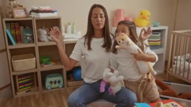 Kızıyla birlikte oyuncaklarla çevrili rahat bir anaokulunda meditasyon yapan bir kadın, evde huzurlu bir aile anı yaratıyor..