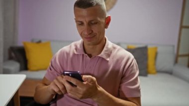 Sarı yastıklı ve modern dekorlu rahat oturma odasında telefonu kullanırken gülümseyen genç bir adam.