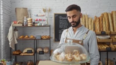 Fırında çalışan sakallı yakışıklı bir adam. Ekmek ve hamur işleri sergileniyor.