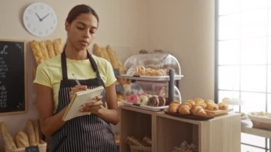 Fırında çalışan genç bir kadın evde sergilenen ekmek ve hamur işleriyle notlar alıyor.