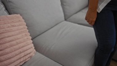 Telefonla konuşan bir kadın oturma odasında gri koltukta oturmuş modern dairede pembe yastıkla konuşuyor.