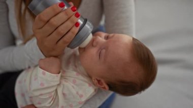 Anne bebeğini şişeyle besliyor. Oturma odasında gösteriş yapıyor. Bakım, sevgi ve evde oturan kadın ve çocuk arasında bağ kuruyor..