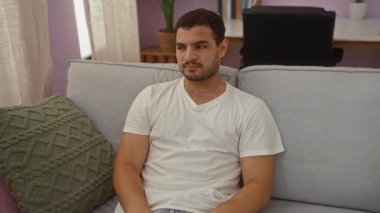 Oturma odasındaki kanepede oturan genç adam kötü kokuya tepki olarak burnunu kapatıyor.