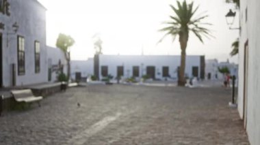Lanzarote 'daki açık hava sahnesinin bulanık arkaplanı, beyaz binalar, palmiye ağaçları ve kaldırım taşı caddeleri olan İspanya, parlak güneş ışığı altında sönmüş ve bokeh etkisini vurguluyor.