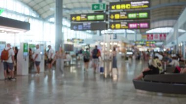 Yoğun havaalanı terminalinde bulanık bir sahne ve arka planda gezginler büyük yön işaretleri altında