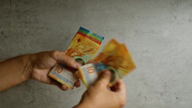 Elele tutuşup saymak. Birçok renkli İsviçre frangı. Beton bir arkaplan üzerinde banknotlar..