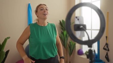 Spor salonundaki akıllı telefondan, spor salonundaki spor aletleri ile yeşil tişört giyen bir kadın.