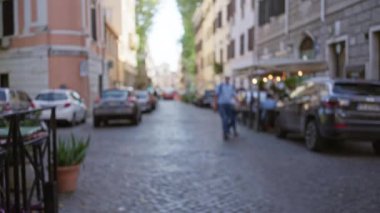 Roma, İtalya 'da kaldırım taşı bir sokakta yürüyen insanların bulanık arabaları ve tarihi binaları öğleden sonra ışığı altında bokeh etkisi yaratıyor..