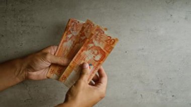 Eller, beton bir yüzey üzerinde birden fazla Filipin pesosu tutuyor.