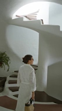 Mirador del Rio Lanzarote 'nin içinde beyaz bir elbise ve gözlük takan bir kadın modern beyaz merdivenlerin yanında arka planda bitkiler olan bir çöp torbası tutuyordu.