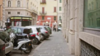 Roma, İtalya 'nın tarihi merkezinde dar bir cadde boyunca park halindeki arabaların ve scooterların bulanık manzarası. Arka planda klasik mimari var..