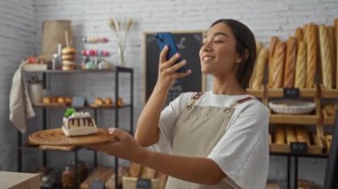 Pasta tutan kadın pastanede fotoğraf çekiyor. Ekmek arka planda. Tatlı ve yiyecek sergiliyor.