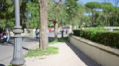 Villa Borghese Bahçeleri 'nde bulanık insanlar güneşli bir günde Roma' da geziniyor, yeşillikleri renklendiriyor ve ambiyansı parkediyor..
