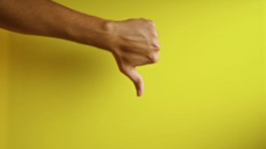 Adamın eli, parlak sarı bir arka plana karşı baş parmak kaldırıyor. Onaylamama ve olumsuzluğu açık ve net bir şekilde gösteriyor..