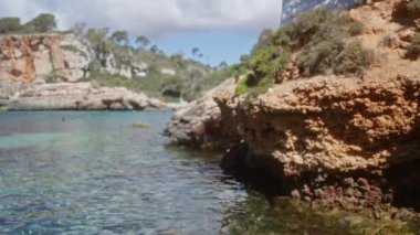 Mallorca İspanya 'daki çözülmüş kayalık kıyı şeridi berrak su, sahil kayalıkları ve açık hava ışığı sergiliyor ve sakin bir sahil atmosferi yaratıyor.