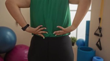 Spor salonundaki spor aletleriyle çevrili kalçaları üzerinde uzanan bir kadın..