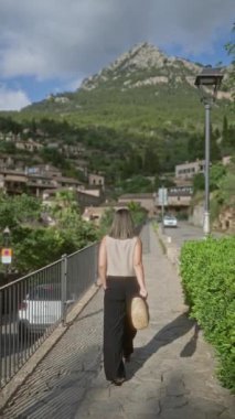 Deia, Mallorca, İspanya 'da, yemyeşil ve dağlık arazilerle çevrili manzaralı bir yolda yürüyen bir kadın.