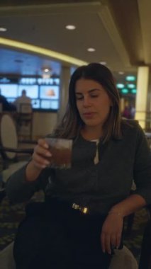 Lüks bar ortamında kokteyl içen bir kadın, arka planda zarif bir iç mekan ve ortam aydınlatması ile rahatlamak ve sosyalleşmek için lüks bir ortam sunuyor..