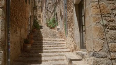 Güneşli bir günde, Mallorca 'nın dar bir ara sokağındaki saksı bitkileriyle dolu kaldırımlı adımlar.