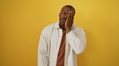 Tek gözü kapalı genç bir adam parlak sarı bir arka plana karşı duruyor, gündelik kıyafetler giyerken cazibe ve gizem hissi yayıyor ve çekici bir ifade sergiliyor..