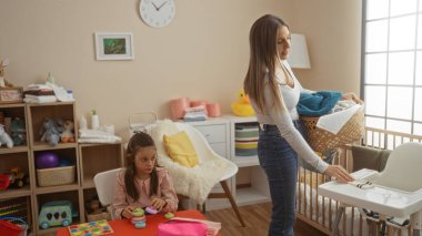 Çamaşır sepeti taşıyan bir kadın, oyuncak ve dekorla dolu rahat oyun odasında oynarken, aile, ilgi, sevgi ve ev hayatını sembolize ediyor..