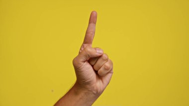 Bir adam elini sarı arka plana doğru kaldırdı. Bu da bir fikir veya noktayı gösteriyor..