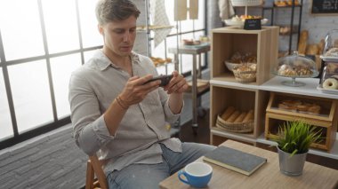 Genç adam, çeşitli hamur işleri ve tatlılarla çevrili fırında akıllı telefon kullanıyor.