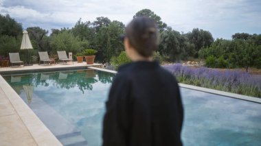 İspanya, Mallorca 'da bir havuzun yanında duran genç kadın yemyeşil ve sakin bir ortam ile çevrili sakin bir adada.