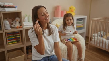 Samimi bir yatak odasında, yanında ksilofon çalan ve sıcak bir aile ortamında gülümseyen bir kızla birlikte telefonundan bir mesaj dinleyen bir kadın..