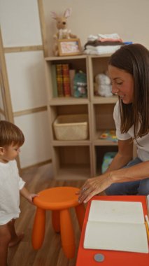 Kadın, oğluyla renkli bir anaokulu oyun odasında etkileşime girer. Sıcak bir ortamda sevgi ve öğrenme ile beslenir..