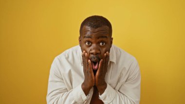 İzole edilmiş sarı bir arkaplan üzerinde şaşırmış bir ifadesi olan yakışıklı genç adam.