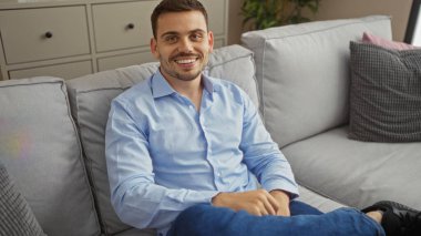 Evdeki modern oturma odasındaki kanepede rahatça otururken sakallı yakışıklı İspanyol adam gülümsüyor..