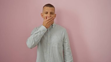 İzole edilmiş pembe arka planda esneyen genç bir adam.